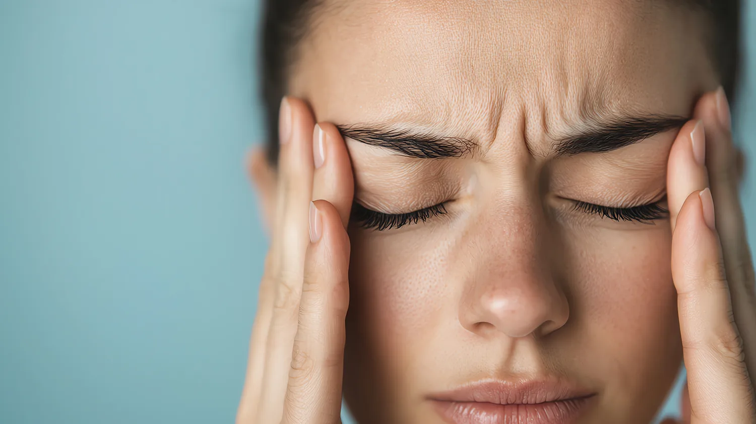 young woman with a stress headache on a teal wall