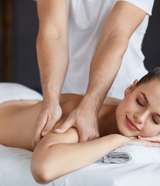 Young beautiful woman enjoying back and shouders massage in spa.Professional massage therapist is treating a female patient in apartment.Relaxation, beauty, body and face treatment concept.Home massage.